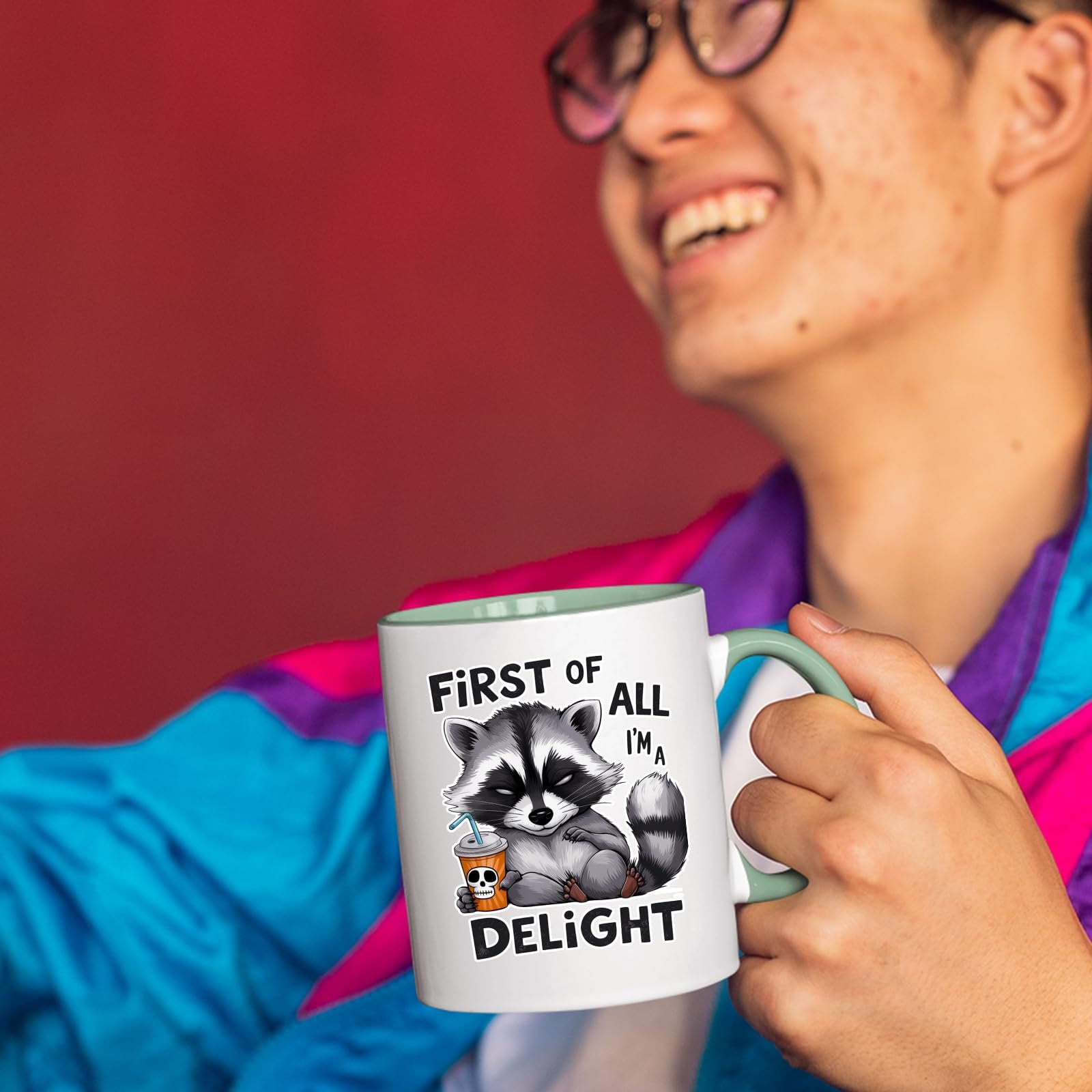 71pa 9ghzjl.jpg Smiling person in a colourful jacket holding the First of All I’m a Delight raccoon mug with a light green handle