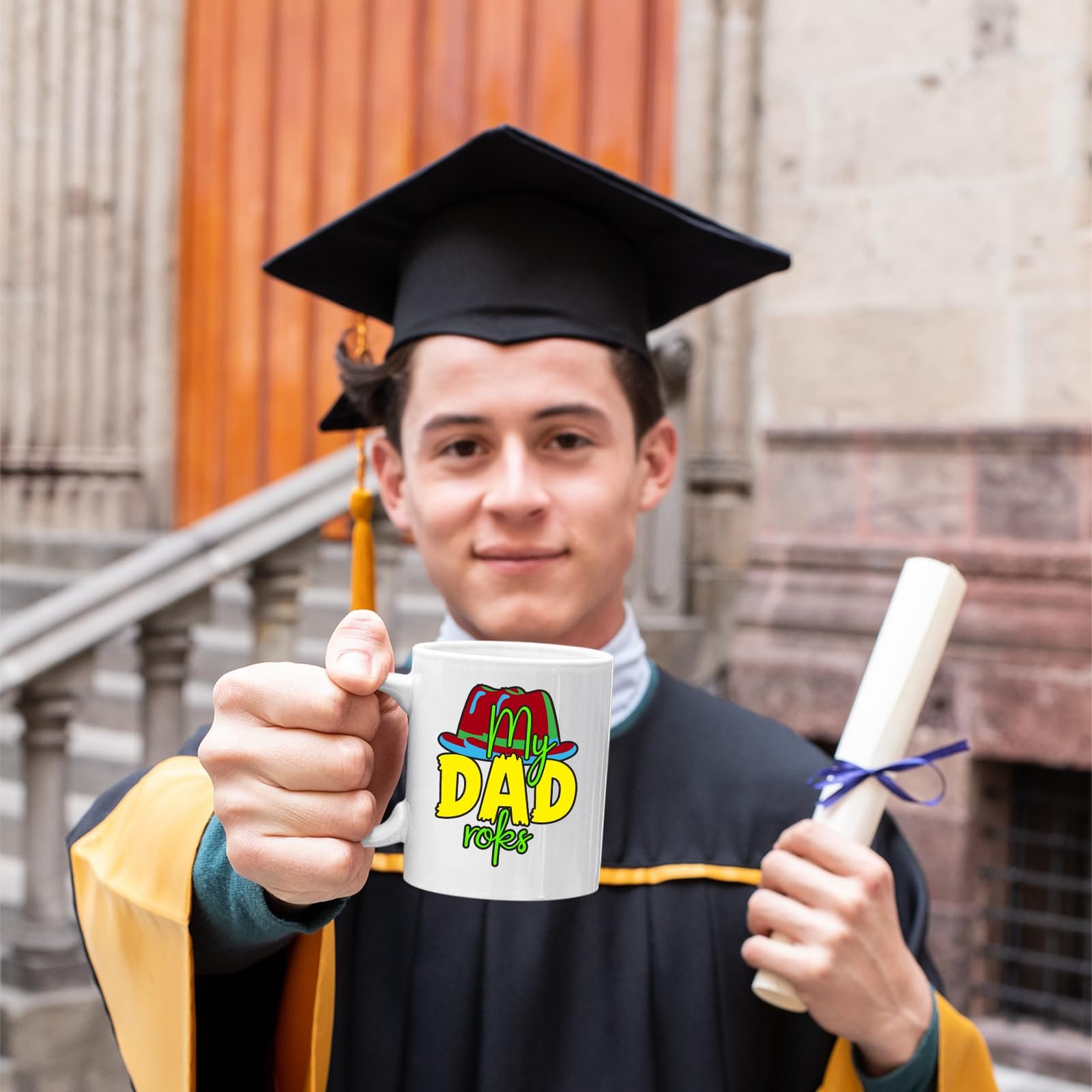 71aqccft6zl.jpg Graduate in a cap and gown holding a mug with the colourful My Dad Rocks hat design