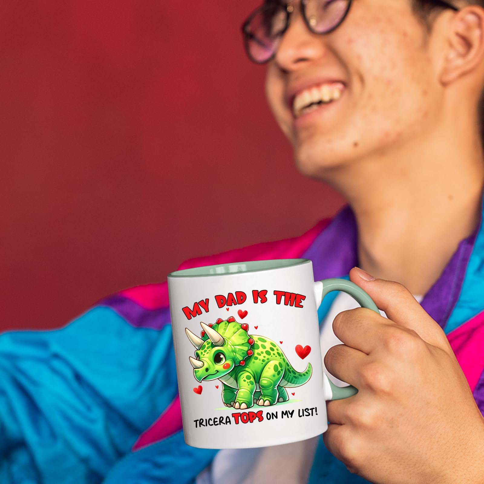 71n3p8mvutl.jpg Smiling person in a colourful jacket holding the Triceratops dad mug with a light green handle