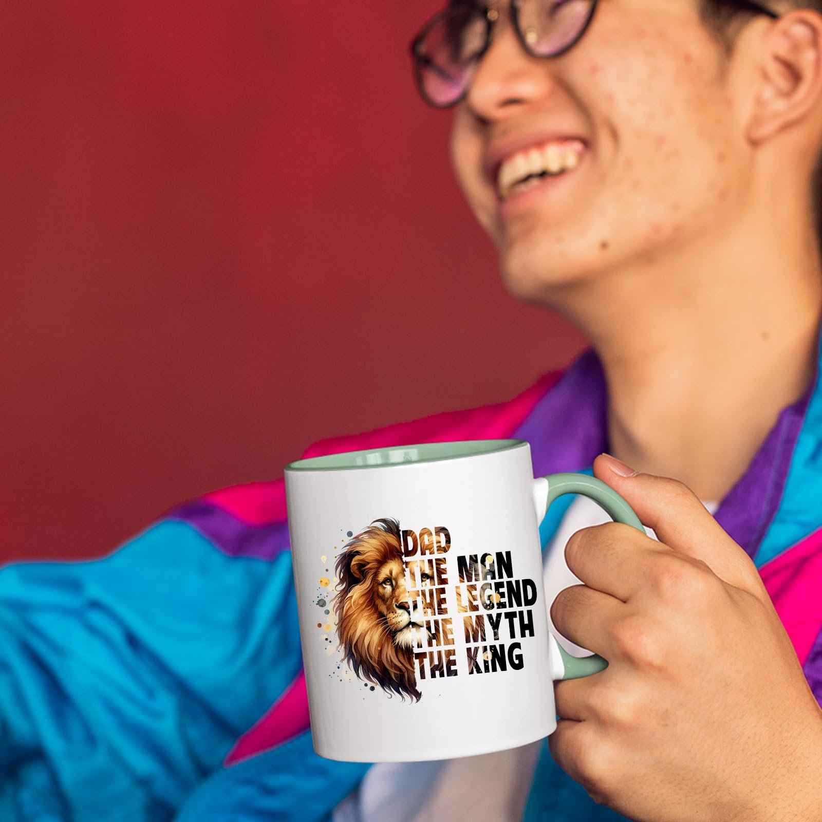 71vequ dgjl.jpg Smiling person in a colourful jacket holding the Dad the King lion mug with a light green handle